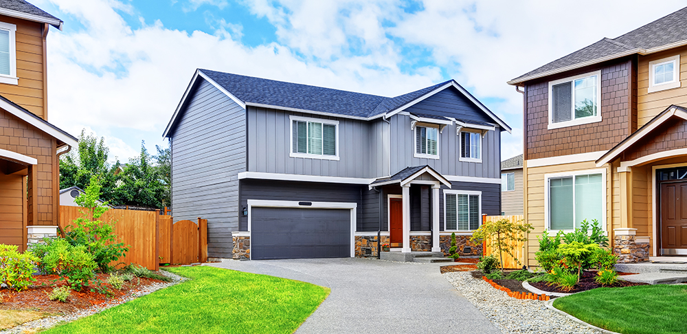 Gray house exterior with dark blue roof and long driveway and two neighboring houses.