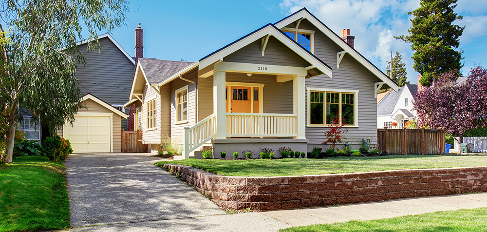 Grey house exterior with front yard landscape. White entrance porch with railings and an orange entrance door.